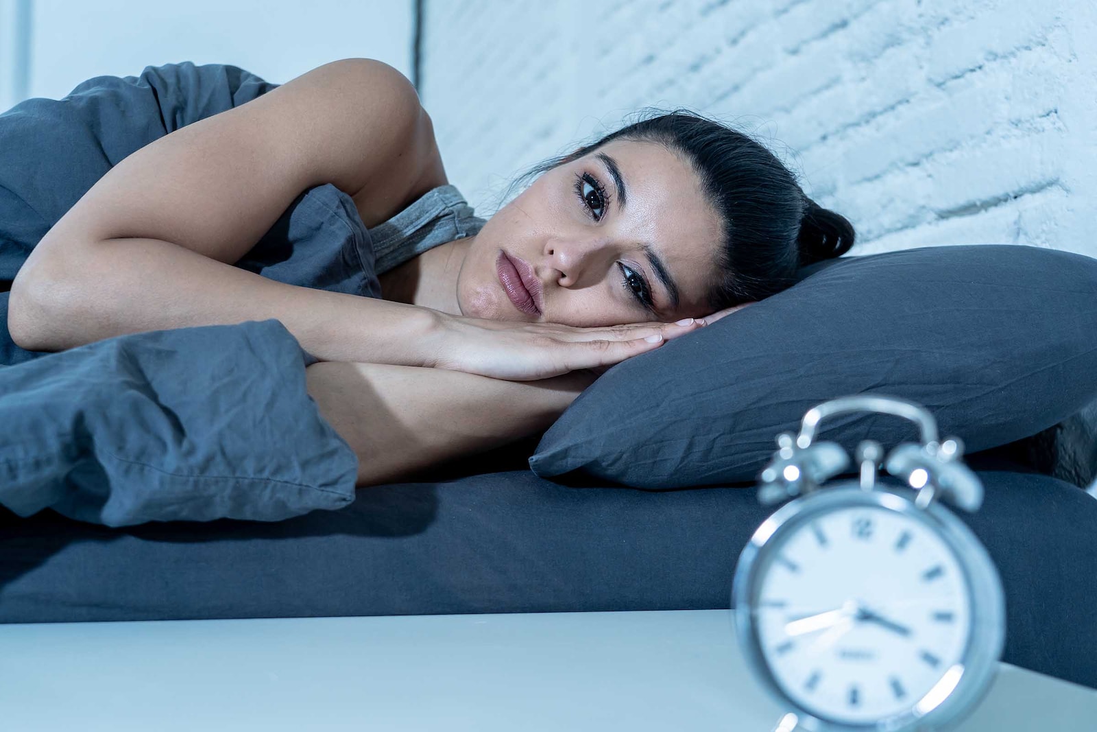 Dona estirada al llit mirant el rellotge amb insomni
