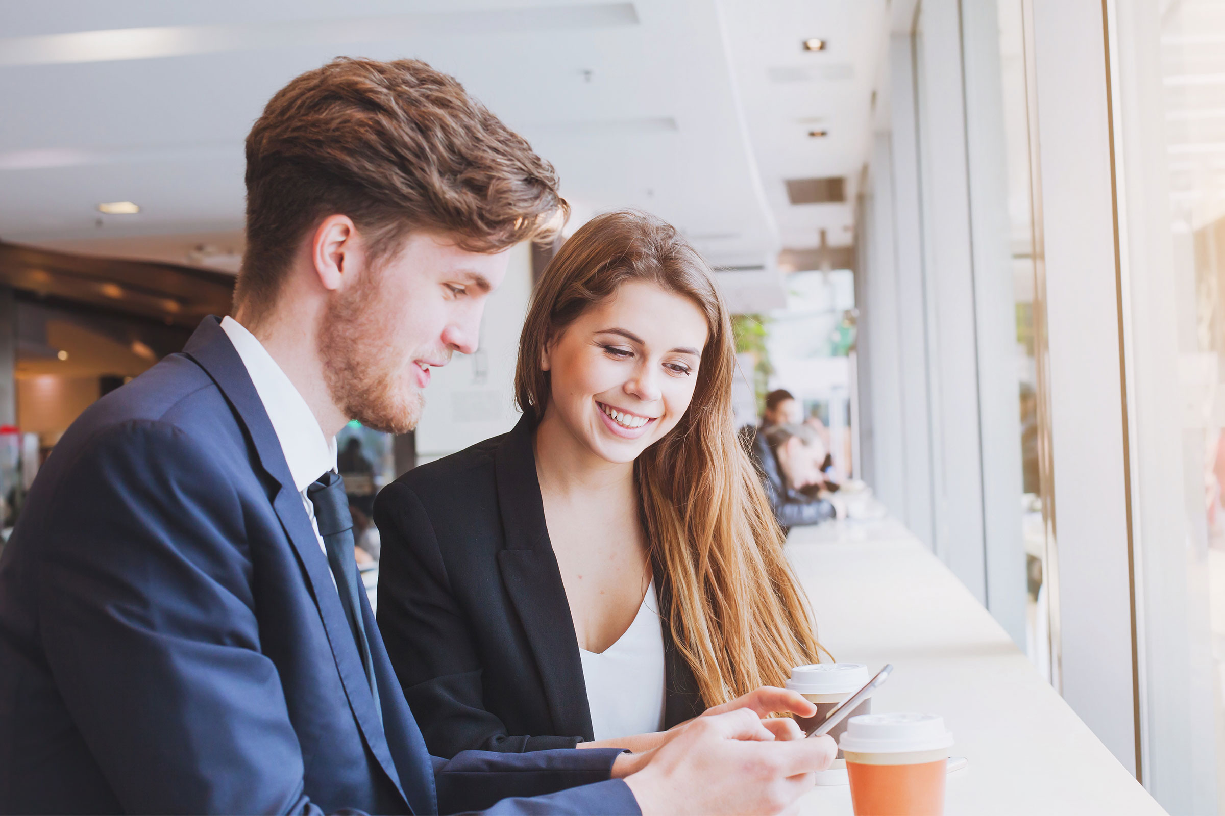 Coworkers getting coffee and looking at their mobile phones together
