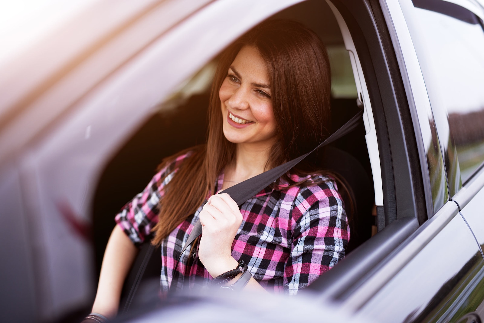 Young woman fastening the seat belt in her new car