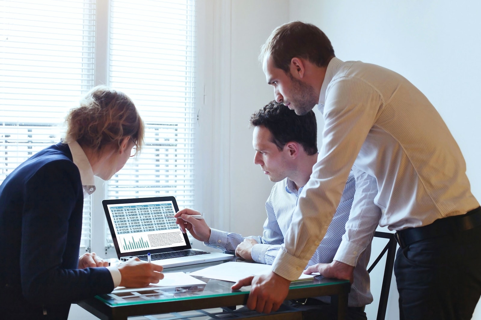 Tres emprendedores conversando en una oficina, frente a un ordenador con los gráficos del negocio, analizando su evolución y los posibles cambios a realizar